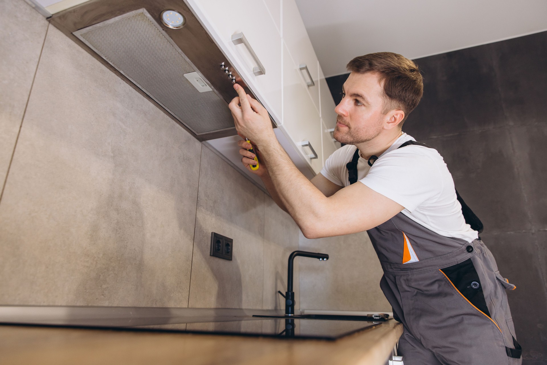 Professional plumber repairing kitchen extractor hood using screwdriver